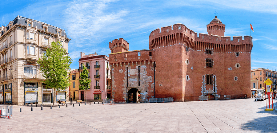 Vue panoramique de la place du château à Perpignan avec des bâtiments historiques et des structures modernes.